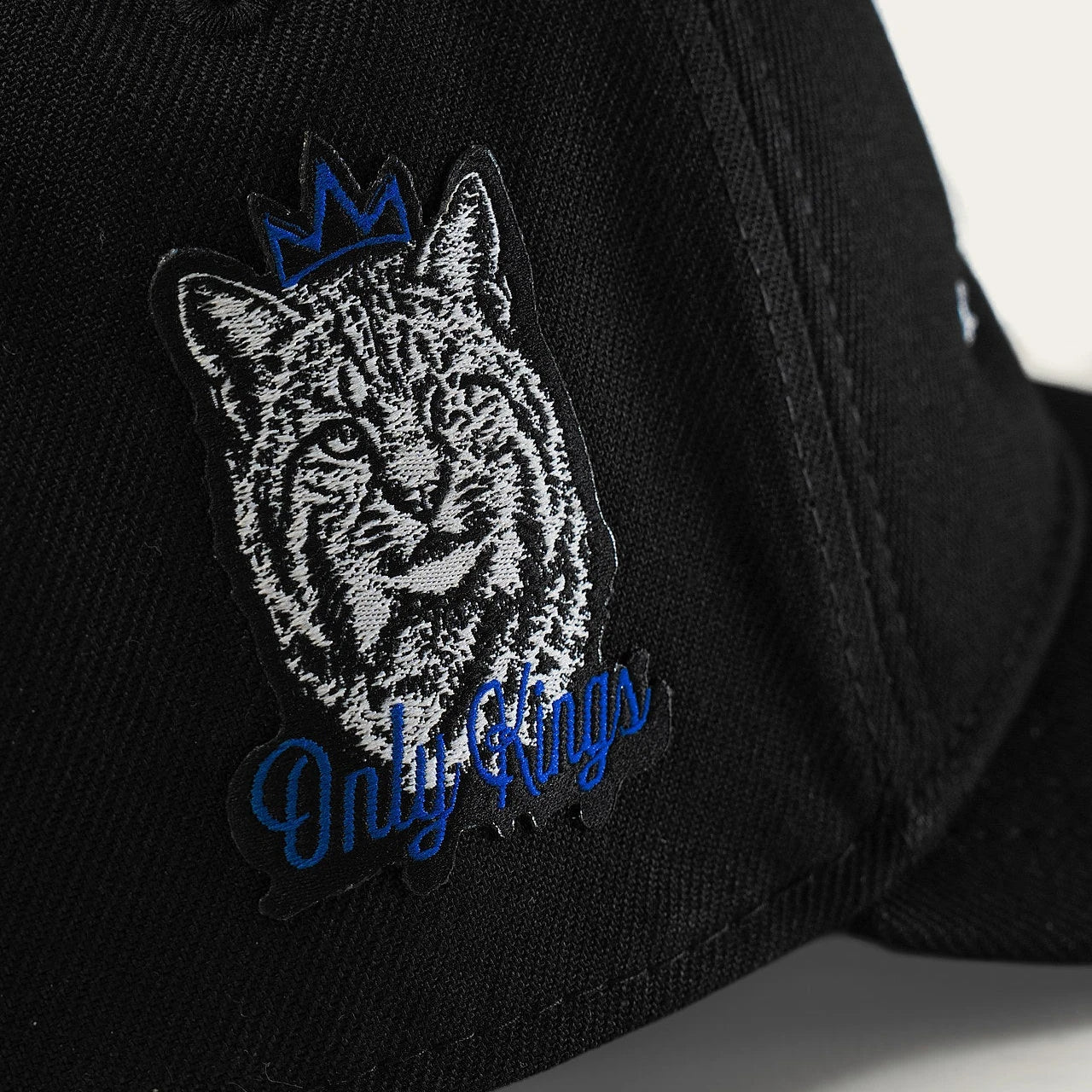 The black cap’s physical side patch shows a white-and-grey Wildcat, a blue outline crown and Only Kings in blue script.